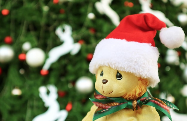 Adorable bebé león de juguete con gorro de Papá Noel con árbol de Navidad borroso en el fondo