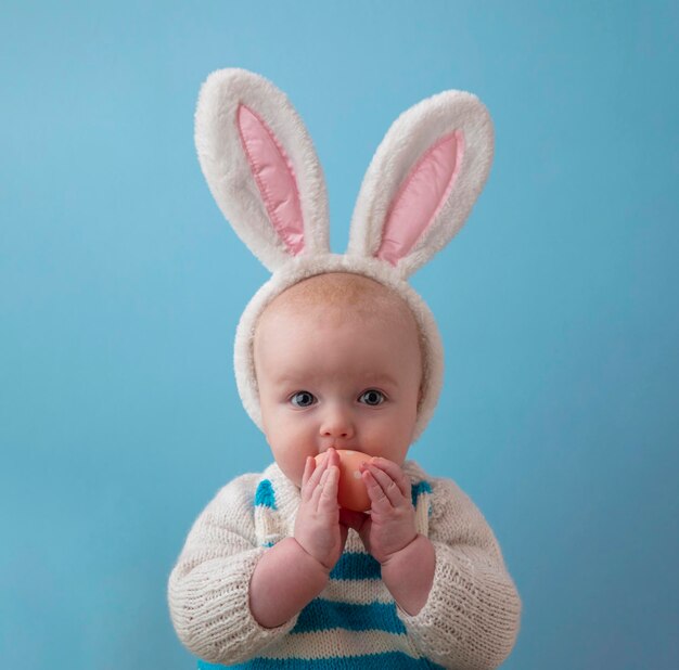 Adorable bebé con orejas de conejo de pascua esponjosas sosteniendo un huevo de pascua