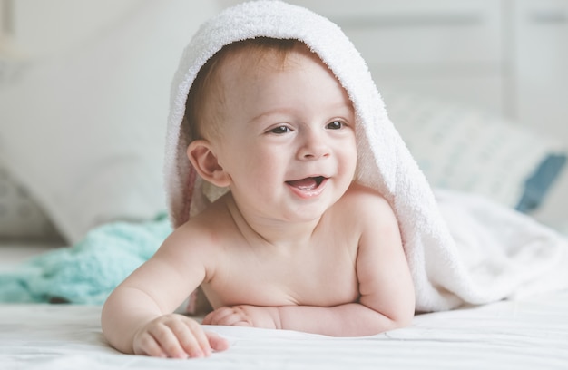 Adorable bebé sonriente en toalla con capucha acostado en la cama después de la hora del baño