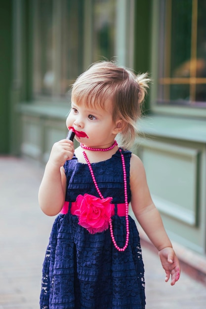 Adorable bebé en un vestido pinta labios con lápiz labial