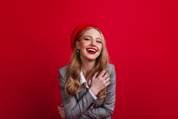 Adorable chica rubia expresando emociones positivas sobre fondo rojo Foto de estudio de risa modelo femenino francés