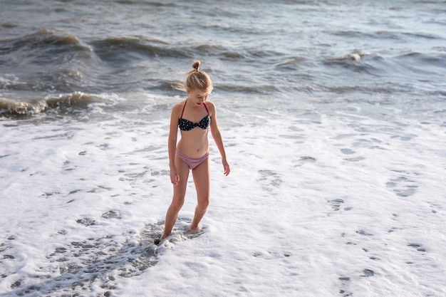 Adorable chica rubia feliz en el traje de baño blanco, rojo y azul en vacaciones en la playa.