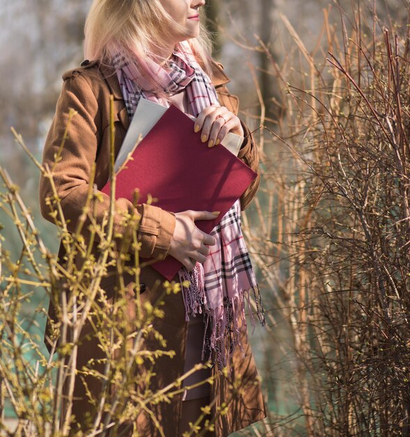 Adorable chica rubia con libros al aire libre Mujer con cabello rosado sosteniendo libro rojo