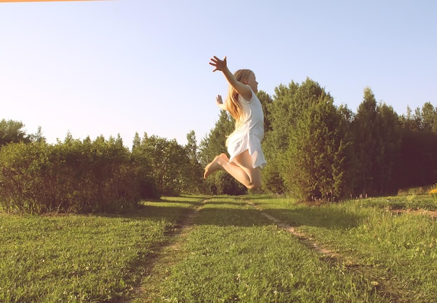 Adorable chica rubia vestida de blanco saltando sobre fondo de naturaleza de verano