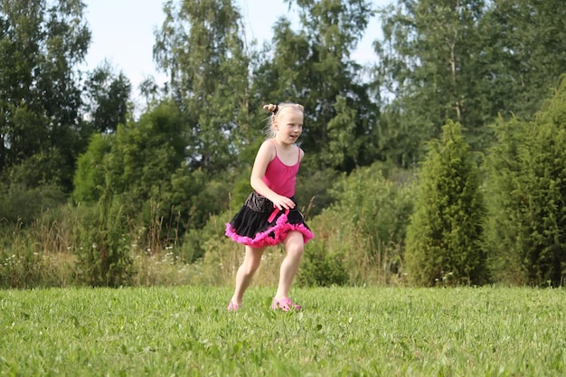 Adorable chica rubia vestida con una pettiskirt jugando y corriendo en un parque de verano en el campo