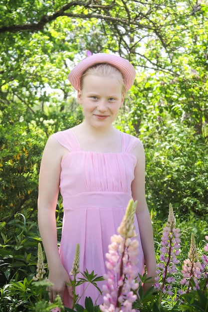 Adorable chica rubia con un vestido rosa y un lindo sombrero en el fondo de la naturaleza de verano en el campo