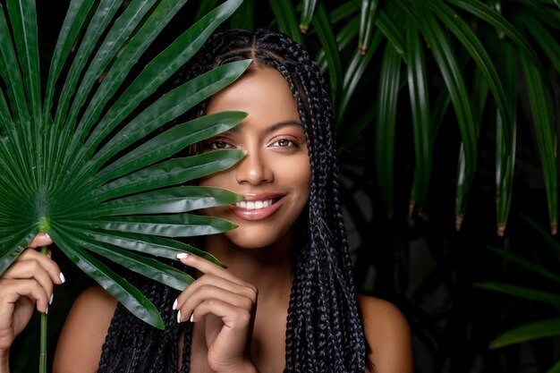 Una adorable dama de raza mixta posando sonriendo en hojas verdes.