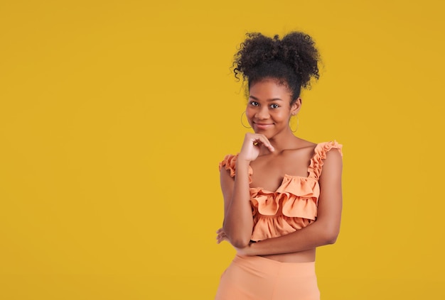 Adorable encantadora mujer de piel oscura usa un vestido de camisa naranja sonriendo fondo de color amarillo aislado