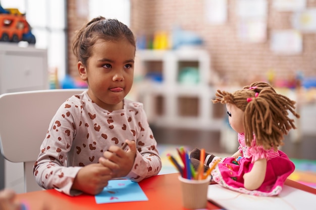 Adorable estudiante hispana sentada en la mesa dibujando en papel en el jardín de infantes