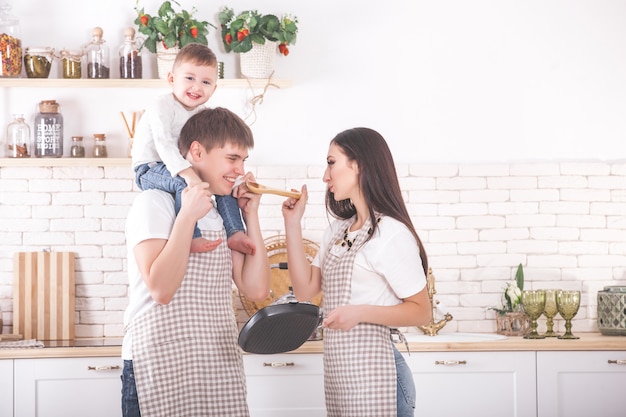 Adorable familia cocinando más lejos. Familia joven en la cocina desayunando o cenando. Mamá, papá y su pequeño hijo preparando comida.