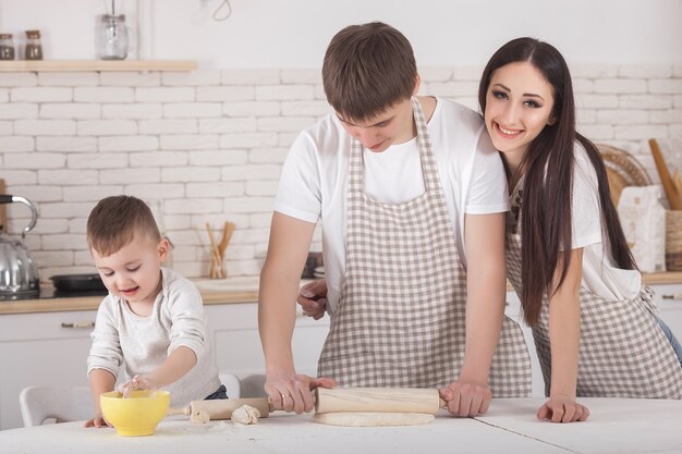 Adorable familia cocinando más lejos. Familia joven en la cocina desayunando o cenando. Mamá, papá y su pequeño hijo preparando comida.