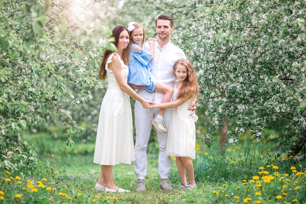 Adorable familia en el floreciente jardín de cerezos en un hermoso día de primavera