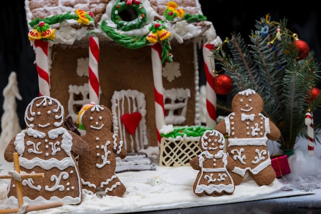 Adorable familia de pan de jengibre cerca de la casa de pan de jengibre casera cubierta de nieve sobre fondo oscuro. Maqueta para ofertas de temporada y postal navideña.