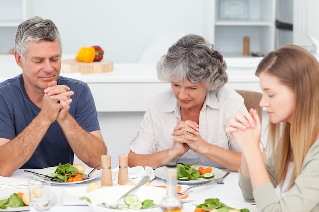 Adorable familia rezando en la mesa