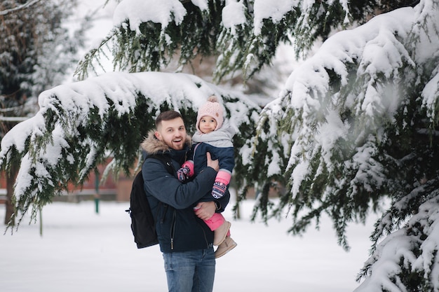 Adorable hijita con su adorable papá junto al gran árbol nevado