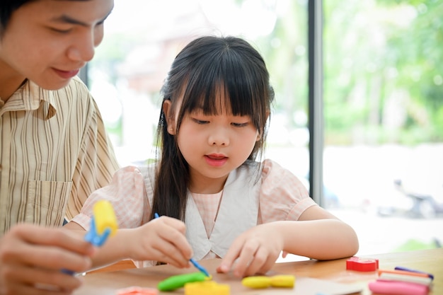 Una adorable joven asiática que se concentra en aprender y esculpir plastilina con su papá