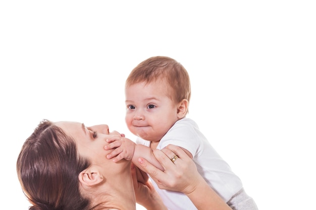 Adorable joven madre sosteniendo a su bebé y mirándolo sobre un fondo blanco.