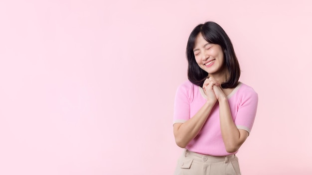 Adorable joven modelo de mujer asiática feliz con emoción tímida expresión sonriente cara atractiva positiva alegre y sosteniendo la mano aislada sobre fondo de estudio rosa pastel Retrato hermosa dama linda