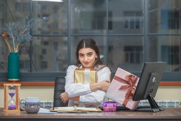 Adorable jovencita abrazando su caja de regalo y mirando a la cámara