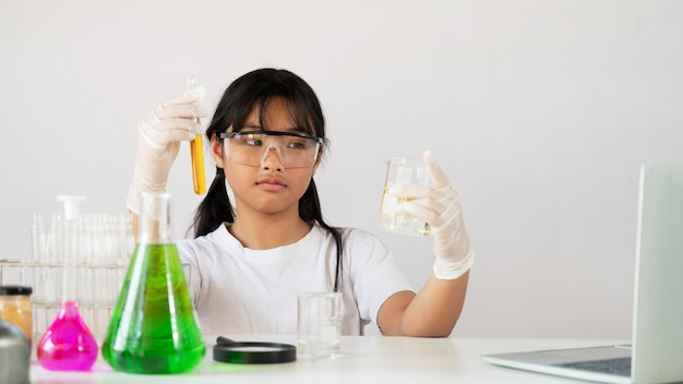 Adorable jovencita en gafas de seguridad y guantes con frascos para química.