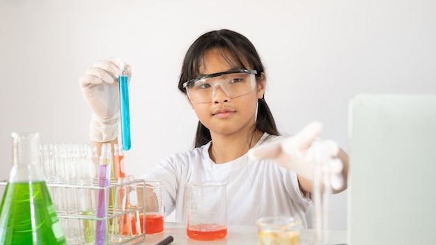 Adorable jovencita en gafas de seguridad y guantes con frascos para química.