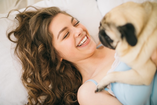 Foto adorable mujer abrazando a su perro pug en la cama