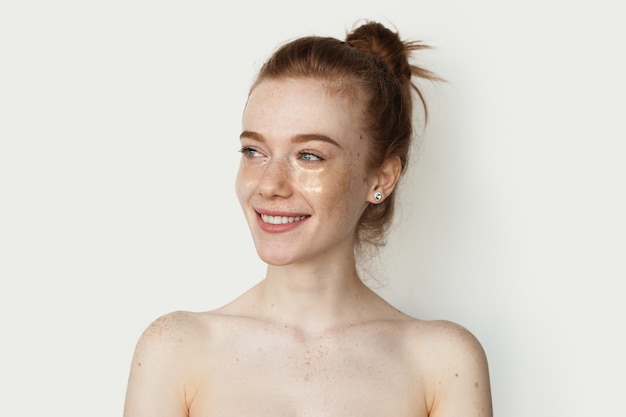 Adorable mujer de jengibre con pecas está sonriendo en una pared de estudio blanco con hidrogel transparente e ...