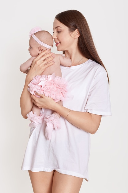 Adorable mujer joven en camiseta blanca con hija en brazos