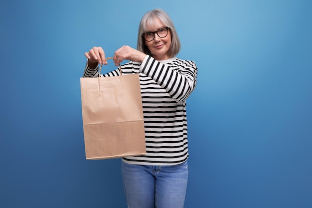 Adorable mujer de negocios madura con cabello gris sosteniendo maqueta de bolsa de compras ecológica en brillante