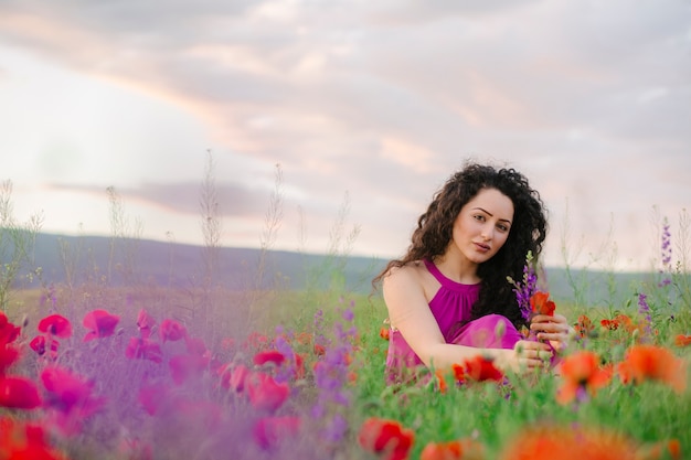 Adorable mujer sentada y disfrutando de la flor de flores silvestres en la pradera