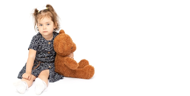 Foto una adorable niña de 2 años abrazando felizmente a su gran oso de peluche bronceado