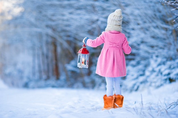 Adorable niña con abrigo cálido al aire libre el día de Navidad con linterna