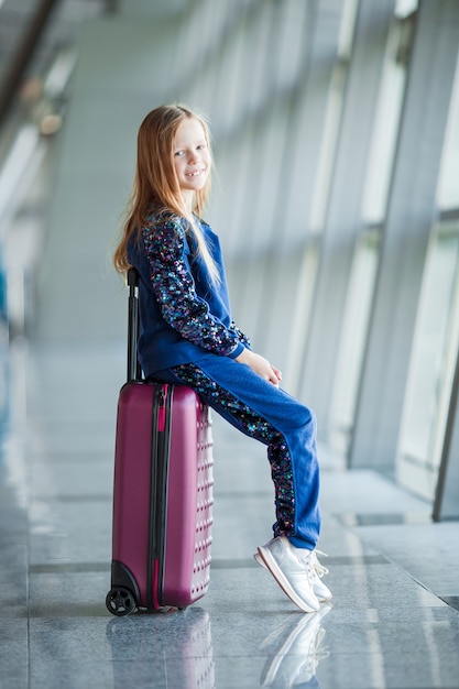 Adorable niña en el aeropuerto con su equipaje esperando el embarque
