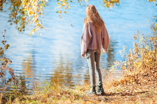 Adorable niña al aire libre en el día de otoño caminando cerca del lago