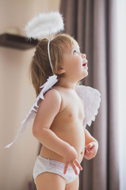 Adorable niña con alas y un halo mira con entusiasmo