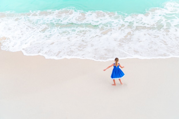 Adorable niña bailando en la playa tropical blanca. Vista desde arriba de una playa desierta con agua turquesa