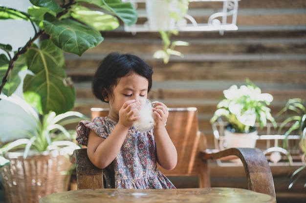 Adorable niña bebiendo leche en la mesa de madera