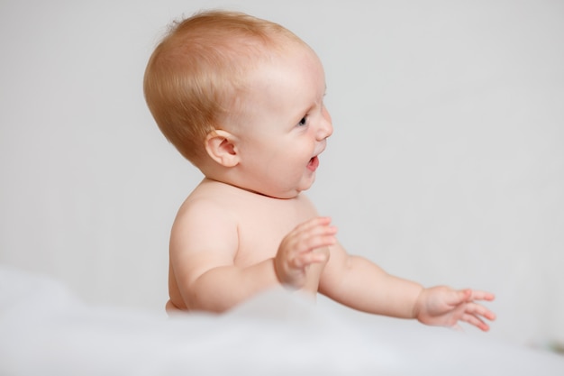 Adorable niña en blanco dormitorio soleado. Niño recién nacido relajante en la cama.