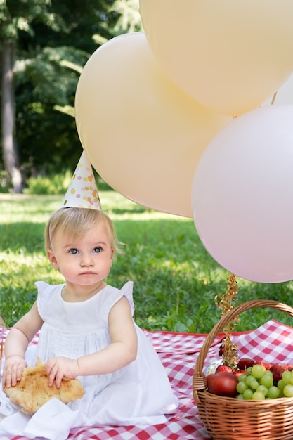 Adorable niña caucásica almorzando celebrando el primer cumpleaños al aire libre en un picnic en verano