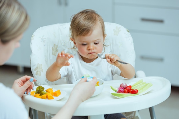 Una adorable niña caucásica come verduras sola pinchándolas con las manos