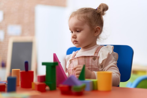 Adorable niña caucásica jugando con bloques de construcción de pie en el jardín de infantes