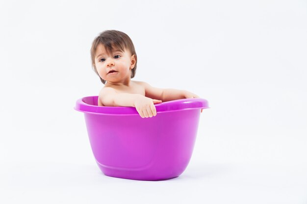 Adorable niña caucásica tomando baño en tina púrpura sobre blanco