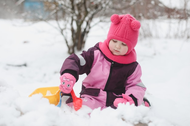 Adorable niña cavar nieve con pala y balde en el patio cubierto de nieve niña jugando en invierno al aire libre