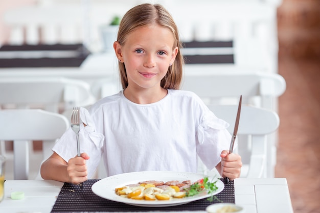 Adorable niña cenando en el café al aire libre