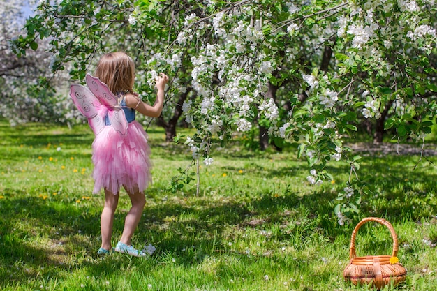 Adorable niña con cesta de paja en floreciente huerto de manzanas