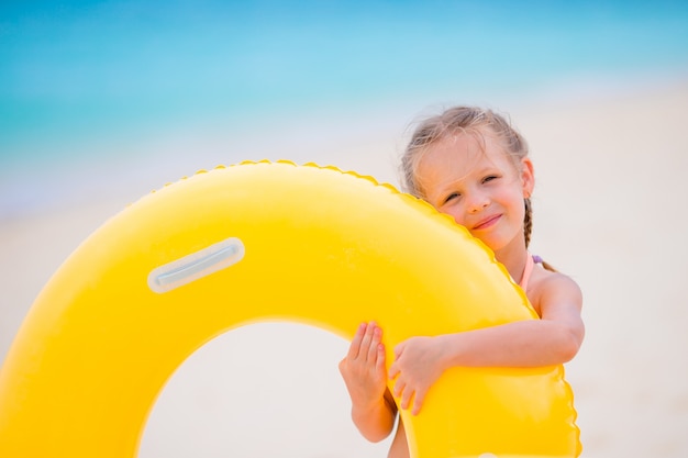 Adorable niña con círculo de goma inflable en la playa blanca lista para nadar