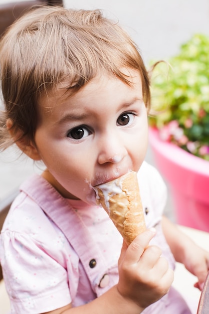 Adorable niña come un helado en la cafetería al aire libre