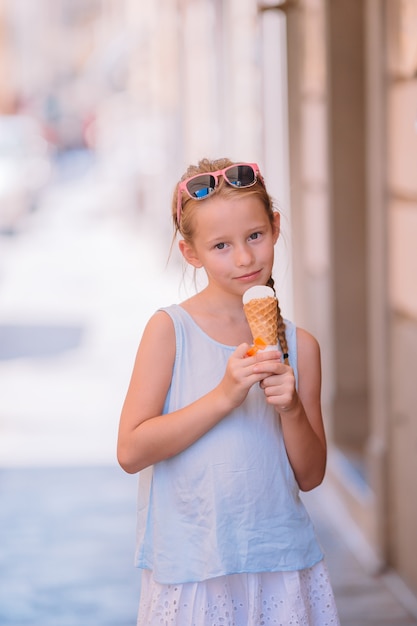 Adorable niña comiendo helado al aire libre en verano.