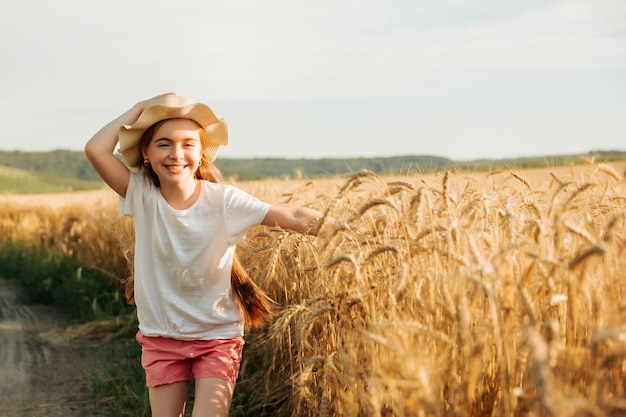 Adorable niña corre alegremente en la carretera cerca del campo de trigo amarillo niño con una forma de vida a