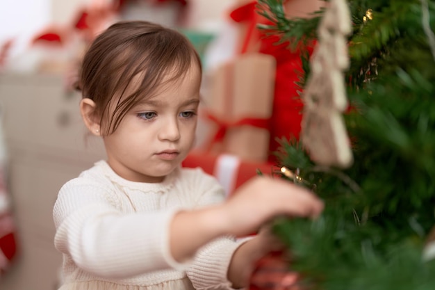 Adorable niña decorando el árbol de navidad de pie en casa